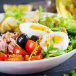 healthy hearty salad tuna green beans tomatoes eggs potatoes black olives close up bowl table